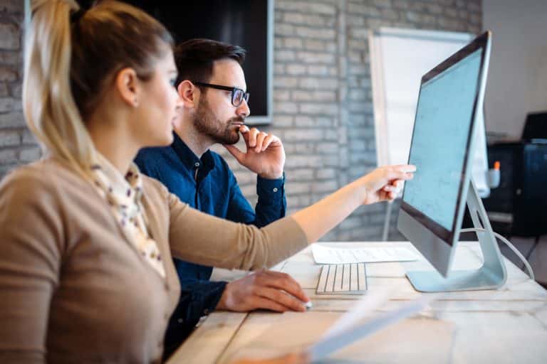 a man and woman looking at an iMac screen and discussing what is on the screen