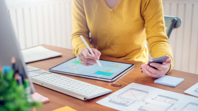 a woman writing on an iPad while holding a phone in her other hand