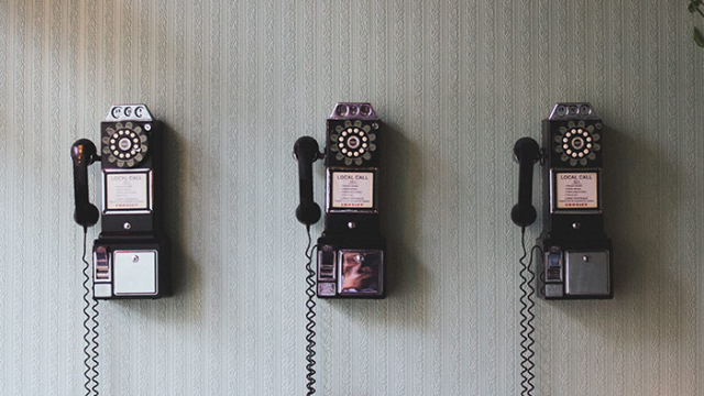 3 old telephones hanging on the wall with wire hanging down