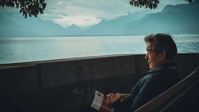 an image of an old man sitting on a bench looking out over a large body of water