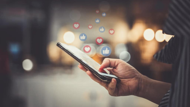 close up of hand holding phone with facebook likes and heart icons streaming out of phone