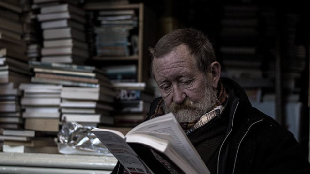 an old man sitting in a dark room full of books while reading a book