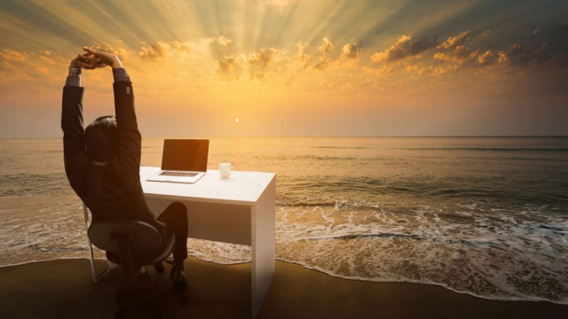 businessman sitting at desk on beach working on redesign of his website
